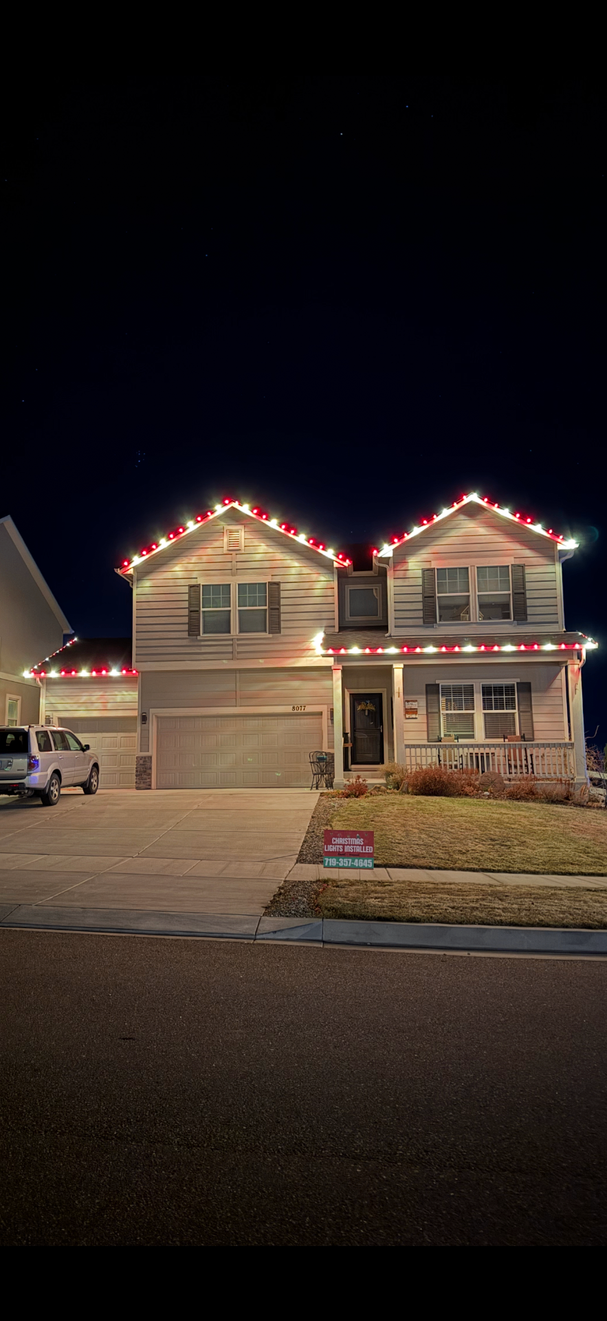 Professional Christmas light installation on two-story home in Colorado Springs, CO featuring red and white LED roofline lights, garage lighting, and festive holiday display completed by expert installers